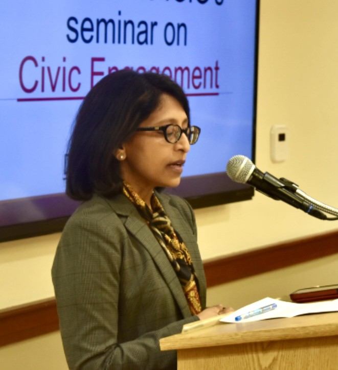 vineeta wearing a business suit and speaking at a microphone at a seminar on civic engagement